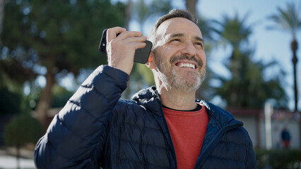 Middle age man smiling confident listening voice message by the smartphone at park