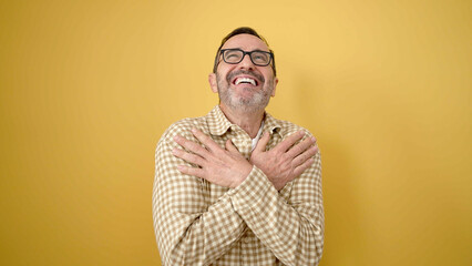 Fototapeta premium Middle age man smiling confident hugging himself over isolated yellow background