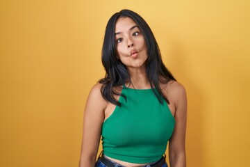 Obraz premium Brunette woman standing over yellow background making fish face with lips, crazy and comical gesture. funny expression.
