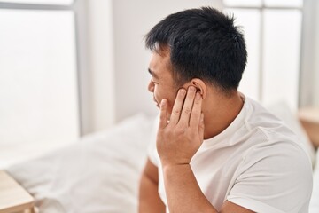 Fototapeta na wymiar Young chinese man suffering for ear pain sitting on bed at bedroom