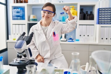 Hispanic girl with down syndrome working at scientist laboratory strong person showing arm muscle,...