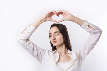 Naklejka premium Portrait of a smiling young woman showing heart gesture with her fingers isolated over white background