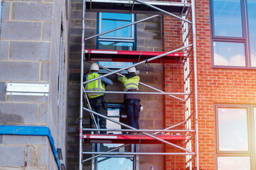 Construction workers using aluminium mobile scaffold tower and safety harness to work at height. Working at height safety regulation - obrazy, fototapety, plakaty