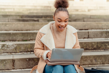 Obraz premium Upset woman student e-learning distance training course study working on stairs in the city. Multiethnic young woman watching online education webinar using a laptop