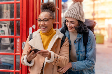 two friend, girlfriend and women using a mobile phone, camera and taking selfie against a red phonebox in the city of England. Travel Lifestyle concept