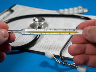 The doctor holds in his hands a thermometer used to measure the temperature of a person's body. Selective focus, close-up.