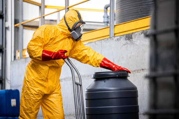 Chemicals factory interior and worker in protective suit and gas mask moving barrel with aggressive or hazardous materials.