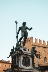 Vertical shot of the Fontana del Nettuno in the centre of Bologna with old buildings in the background in a sunny evening