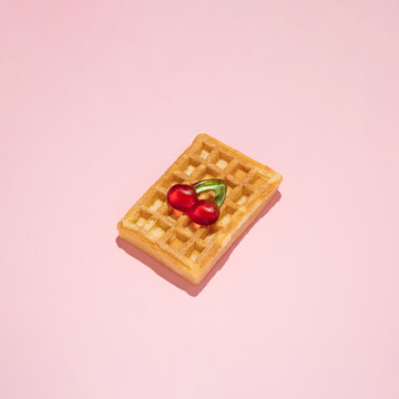 Fresh waffle with gummy candy shaped like cherry on pink background.