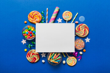 Flat lay holiday composition. Paper blank, lollipop, birthday decorations on Colored background. Top view, copy space for text