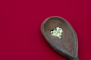 Wood spoon with a heart shaped hole filled with low dosage aspirin isolated on a red background. Concept heart health