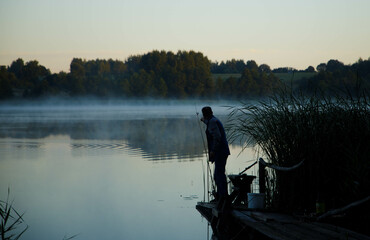 Fisherman at dawn, foggy lake, dark time of day.