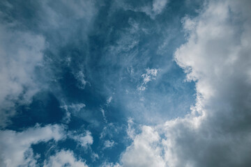 Intense blue sky with fluffy white and greyish storm clouds and intense midday light