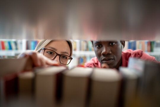 Interested focused multinational students look for needed information in library books while prepare for exam or project together. Couple picking literature for education checking order in books store