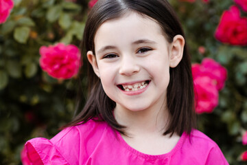 Smiling child girl 7-8 year old show her new  permanent teeth in dental smile over nature floral background outdoor. Look at camera. Healthcare. Childhood.