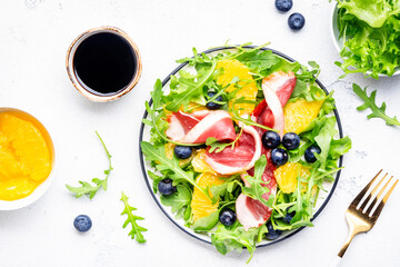Gourmet salad with smoked duck, oranges, blueberries, arugula and lettuce and balsamic vinegar, white table background, top view