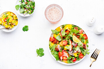 Fresh salad with grilled chicken slice with mango salsa, tomato, cilantro, red onion and lettuce in mexican style, white table background, top view