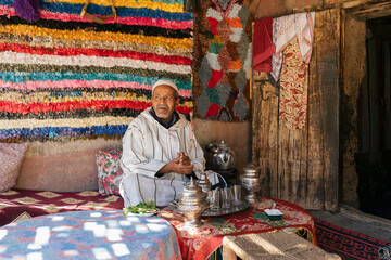 Elderly Berber man sitting on the terrace of his house preparing a tea. Traditional arabic hospitality.