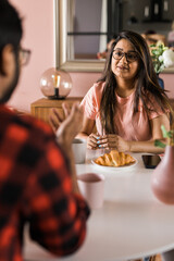 Happy indian couple having breakfast and small talk together in the kitchen - friendship, dating and family