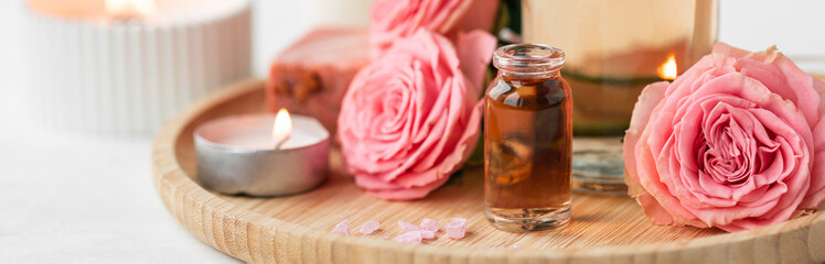 Aromatherapy. Pure organic essential rose oil concept. Elixir with plant based floral herbal ingredients. Pink flowers extract. Spa atmosphere with candle, towel. White background. Banner copy space