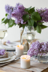 Obraz na płótnie Canvas Beautiful table decor for a wedding dinner with a spring blooming lilac flowers. Celebration of a special marriage holiday event. Fancy white plates, wineglasses, candles. Countryside style
