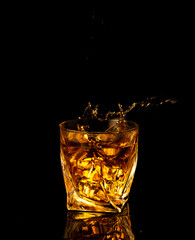 Pouring alcohol and throwing an ice cube into a glass with splashes on a black background