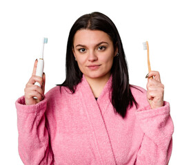 A woman in a pink bathrobe holds both an electric toothbrush and a traditional toothbrush, with a...