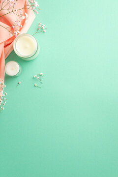 Hello spring concept. Top view vertical photo of candles in glasses gypsophila flowers and pink scarf on isolated teal background with copyspace