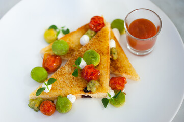Close-up of Avocado Toast on a white plate. Two bread triangles with fruit scoops, cream cheese, sundried tomatoes, chives, ketchup on glass. Breakfast food, recipe, cafe, restaurant menu background.