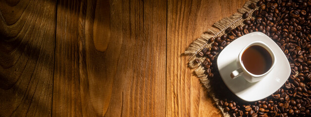 Coffee break background. Hot coffee in cup and roasted coffee beans on a wooden table. Copy space