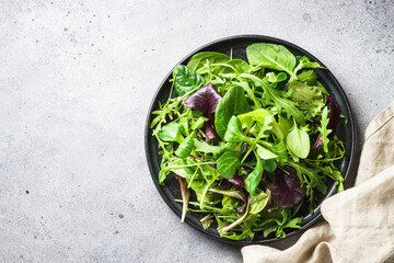 Fototapeta na wymiar Green salad with fresh leaves in black plate. Healthy food, clean eating, diet. Top view.