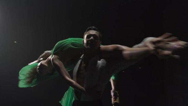 Dance support in rotating around close up. Man holds woman on his shoulders parallel to floor, her legs in arabesque. Camera tracking