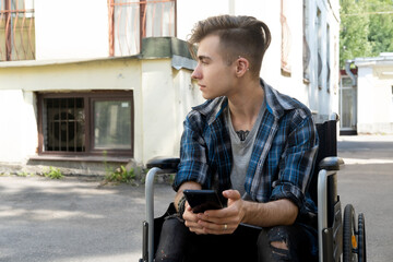 A young disabled man sits in a wheelchair and listens to music on headphones. Walk on a summer day....