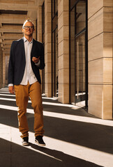 Young elegant handsome man dressed casual go by next to columns of an modern big building