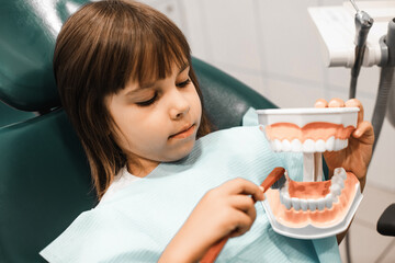 Child girl after the doctor at the clinic, holding a dental jaw and brush teeth in her hands