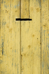 Fridged old boards with shabby yellow paint. Part of the old wooden fence in rural areas. A hole for letters