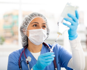 Female nurse in a protective mask, working in the clinic in the treatment room, fills a syringe with medicine with ..saline solution for injection