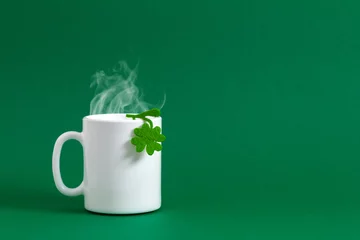 Deurstickers Saint Patricks Day background. White cup of hot tea or coffee with steam for St. Patrick's day, mug, green paper clover leaf on green background. Front view © prime1001