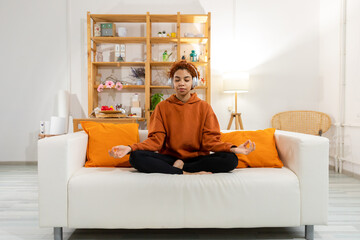 Yoga mindfulness meditation. Young healthy african girl practicing yoga at home. Woman sitting in lotus pose on yoga mat meditating smiling relaxing indoor. Girl doing breathing practice, yoga at home