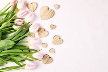 A bouquet of pink tulips next to wooden hearts on a pink background with space for text. Greeting card for valentine's day or mother's day