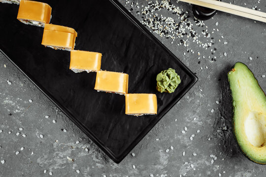Traditional fresh japanese sushi rolls on a black stone Teka Kaji. Roll ingredients: cheese cheder, philadelphia cheese, cucumber, tuna chips, nori, rice