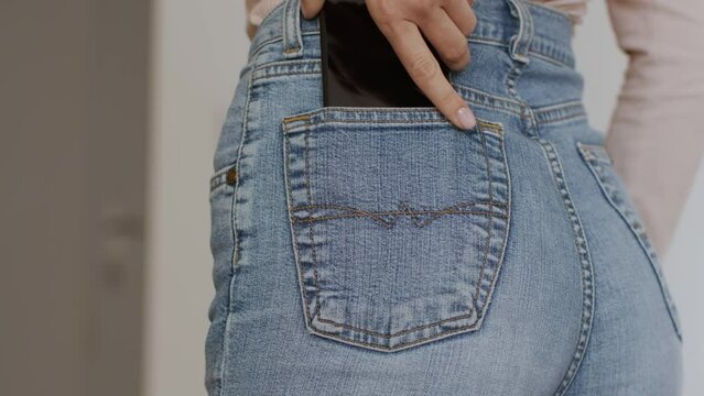 Close up shot of unrecognizable women's hand put mobile phone into her trendy blue jeans pocket, back view, empty space