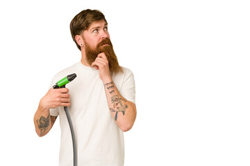 Adult man holding a watering hose isolated looking sideways with doubtful and skeptical expression.