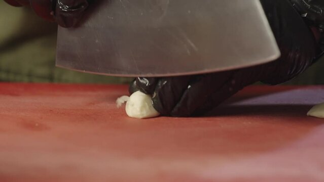 A chef is chopping a clove of garlic on a cutting board in the kitchen. Preparation of ingredients by a professional for cooking in a restaurant.
