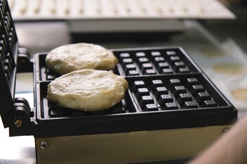 Close-up chef pours waffle batter in a waffle iron in a professional kitchen. Waffle making at the hotel with all-inclusive meals. belgian waffles in a waffle iron.
