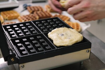 Close-up chef pours waffle batter in a waffle iron in a professional kitchen. Waffle making at the...