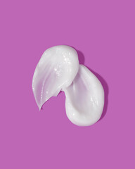 White beauty cream smear smudge on purple background. Cosmetic skincare product texture. Face cream, body lotion swipe swatch