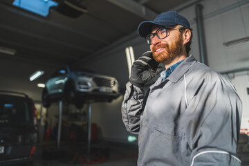 cheerful auto mechanic talking on a phone at job and smiling, medium shot. High quality photo