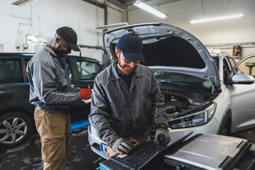 Fototapeta na wymiar two professional servicemen making car diagnostics on a laptop and smiling, medium shot car repair shop. High quality photo
