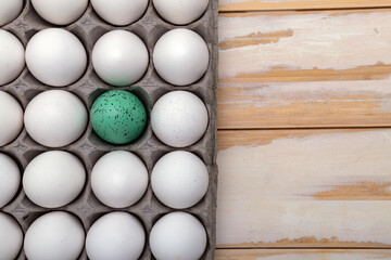 white raw eggs in a container and one easter egg. Preparing for the holiday of light Easter. View from above. Space for text.